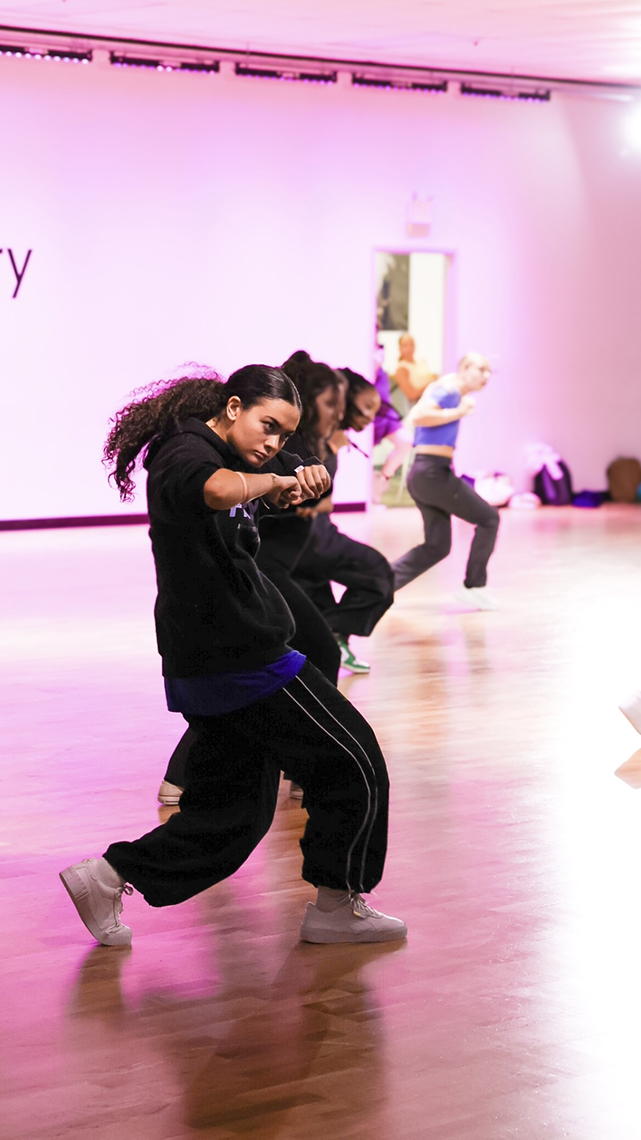 Jordan leads a group of dancers in a pink walled dance studio into a krumping hip hop routine