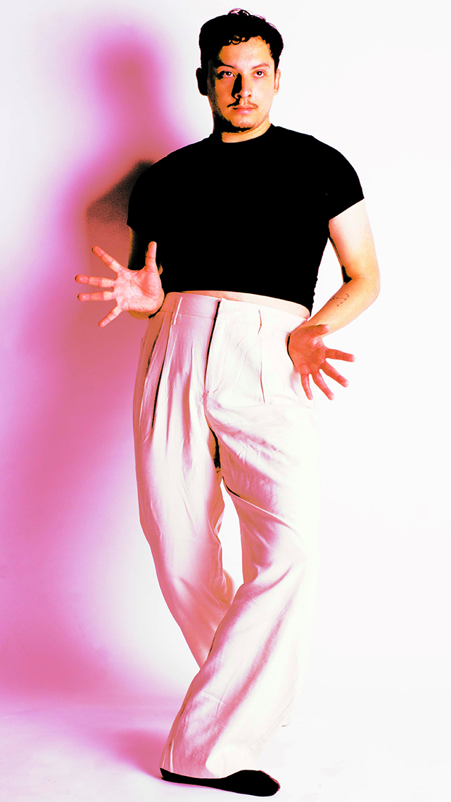 Dancer Jonathan Gerardo in baby pink dance pants and black fitted top does a cross over pose with jazz hands