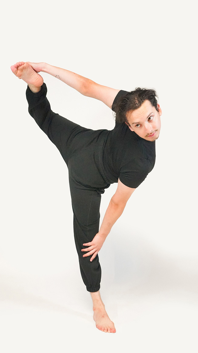 Jonathan Montoya Gerardo in all black dance outfit gets ready to do an leg hold turn by holding foot