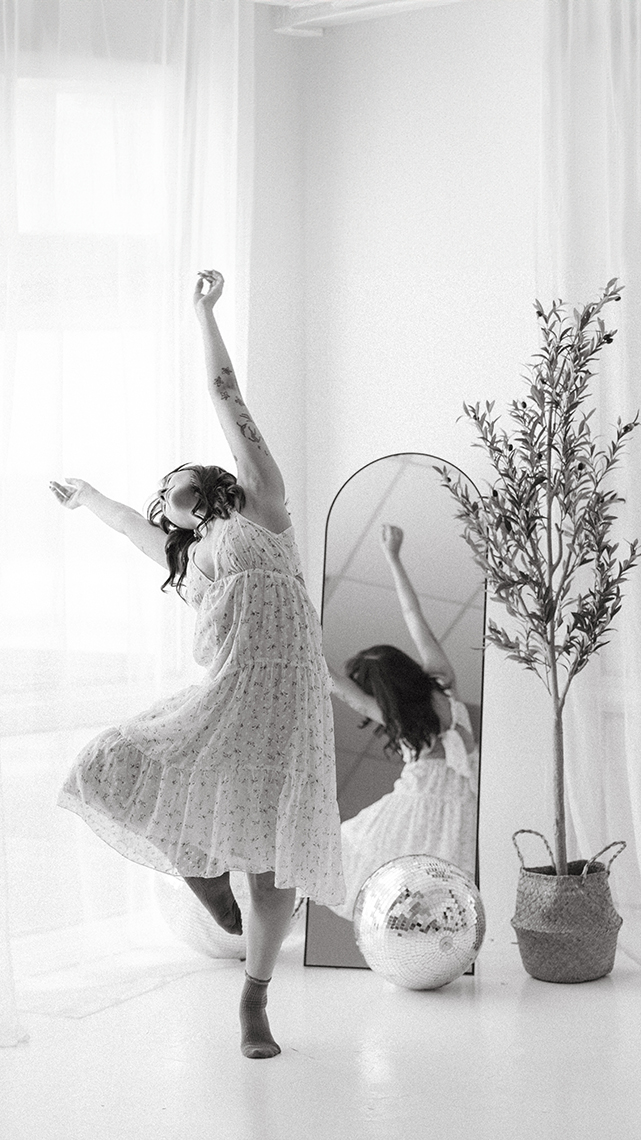 Kiera in a white tiered dress with socks on does a ballet leg lift