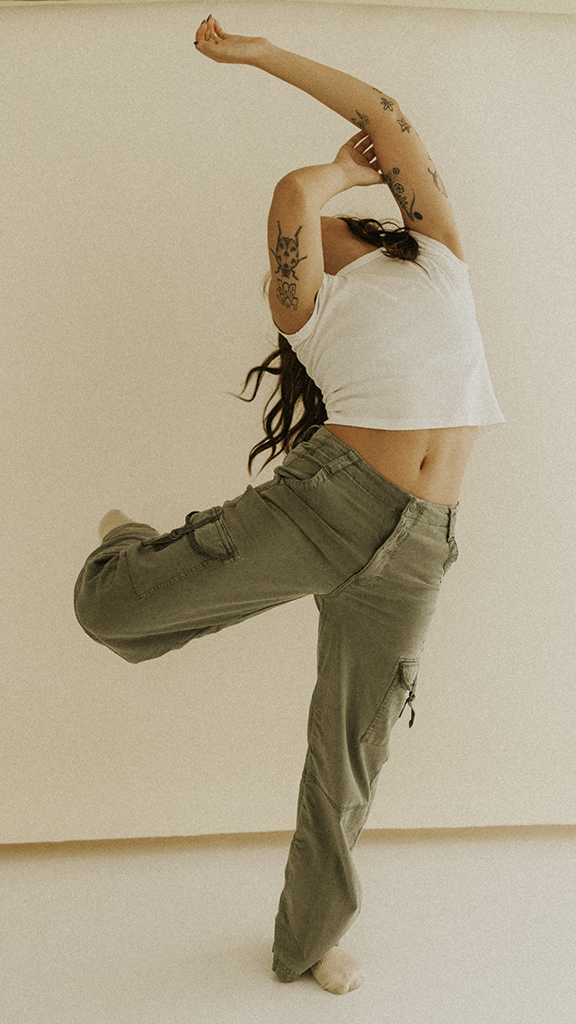 Kiera in a white tee and olive pants does a lyrical back leg left and extended backward arm movement