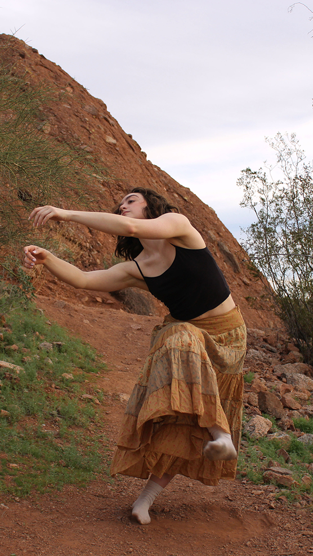 Dancer in black tank top and tan tiered skirt and socks does dance on trail